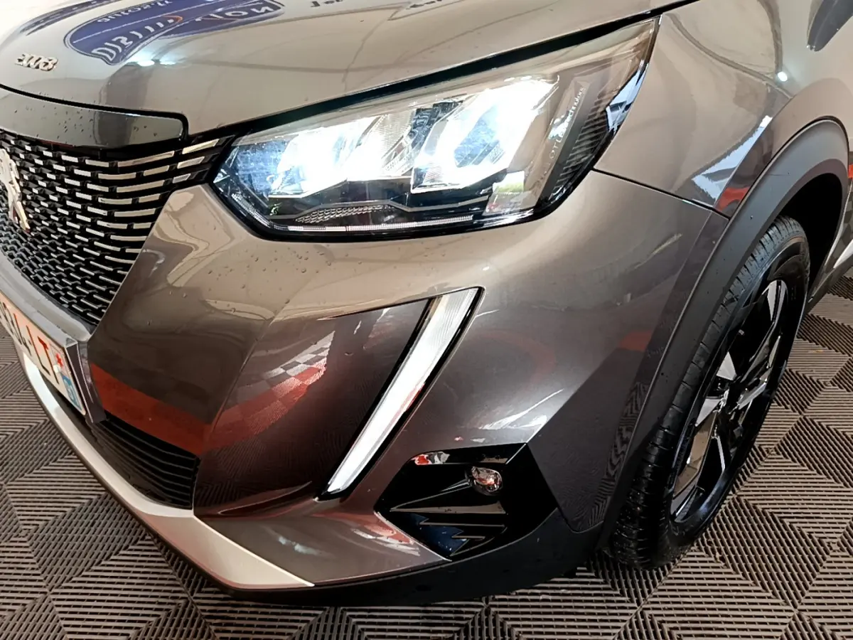 Gros plan sur l'avant droit gris foncé du Peugeot 2008 2022 avec phares LED allumés et jante noire brillante.