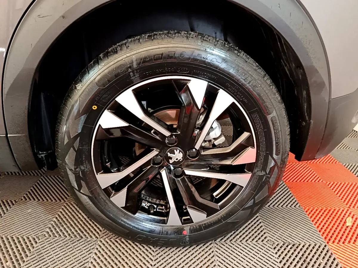 Gros plan sur la roue avant droite du Peugeot 2008 gris foncé, mettant en valeur la jante noire et argentée au design moderne.
