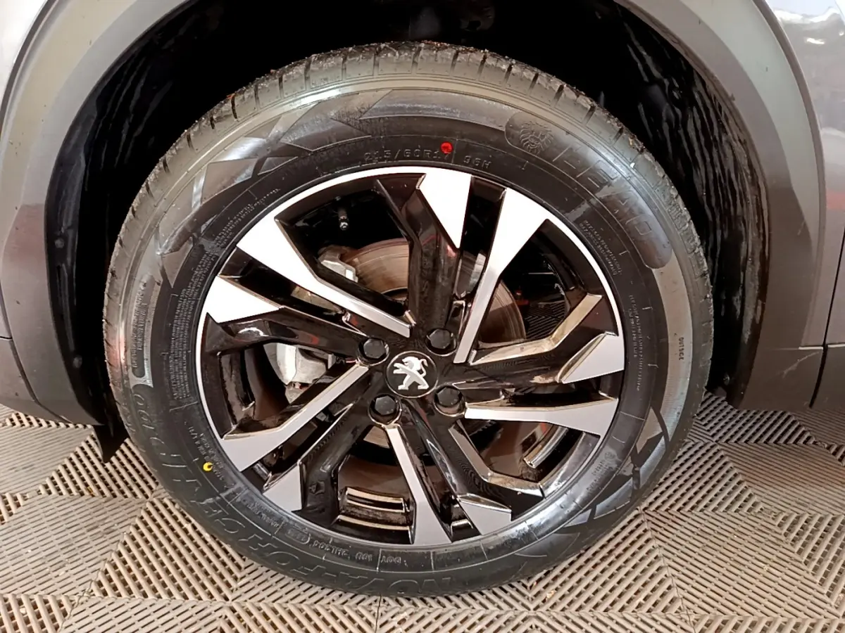 Gros plan sur la roue avant droite du Peugeot 2008 gris foncé, avec jante alliage noire et argentée au design moderne.