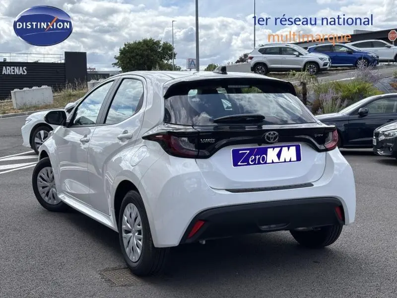 Toyota Yaris 116h Dynamic blanc vue 3/4 arrière droit, avec hayon noir et feux arrière intégrés au bandeau noir.