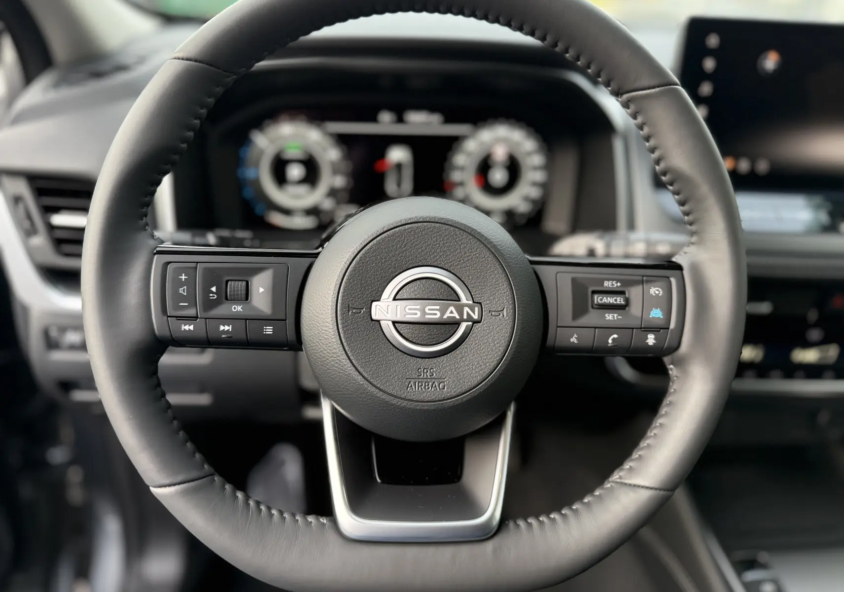 Vue rapprochée du volant cuir noir du Nissan Qashqai 2025 avec commandes intégrées et tableau de bord numérique flou en arrière-plan.