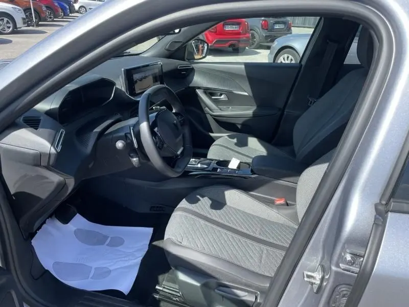 Vue intérieure côté conducteur du Peugeot 2008 gris métal 2025, montrant le tableau de bord moderne et les sièges tissu gris.