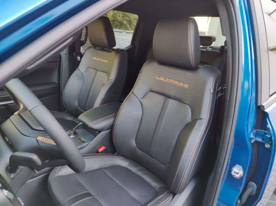 Vue intérieure côté conducteur du Ford Ranger Wildtrak bleu lightning, sièges cuir noirs avec surpiqûres orange et logo Wildtrak brodé.