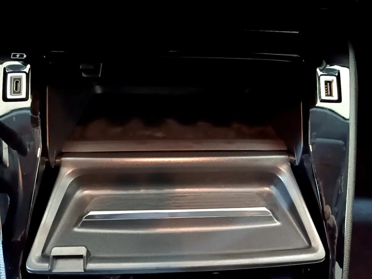 Vue rapprochée de la boîte à gants ouverte avec ports USB et finition noire brillante dans une Peugeot 208 gris foncé.