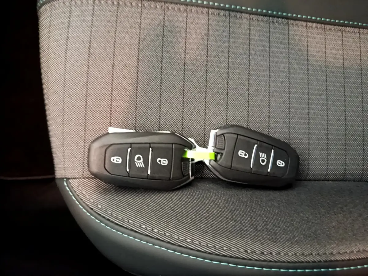 Gros plan sur deux clés noires posées sur un siège gris foncé avec surpiqûres bleues, intérieur Peugeot 208.