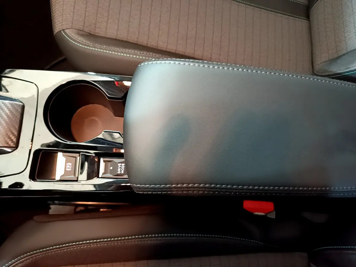 Gros plan sur la console centrale noire et accoudoir cuir gris foncé de la Peugeot 208 PureTech 2022, sièges tissu beige.