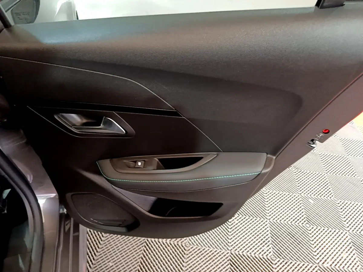 Vue intérieure du panneau de porte côté gauche de la Peugeot 208 gris foncé avec surpiqûres bleues et commande de fenêtre.