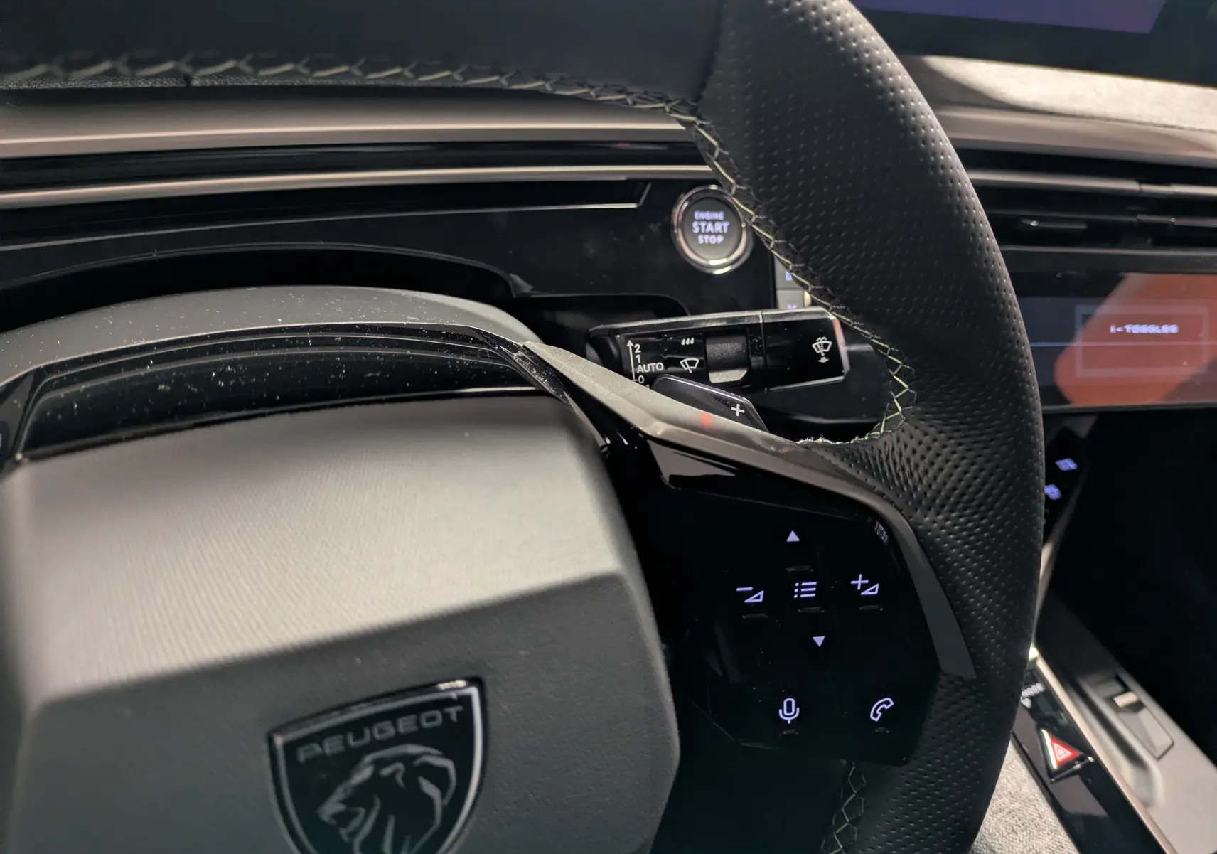 Vue rapprochée du volant cuir perforé noir du Peugeot 3008 Hybrid 145 GT avec commandes tactiles et bouton start/stop.