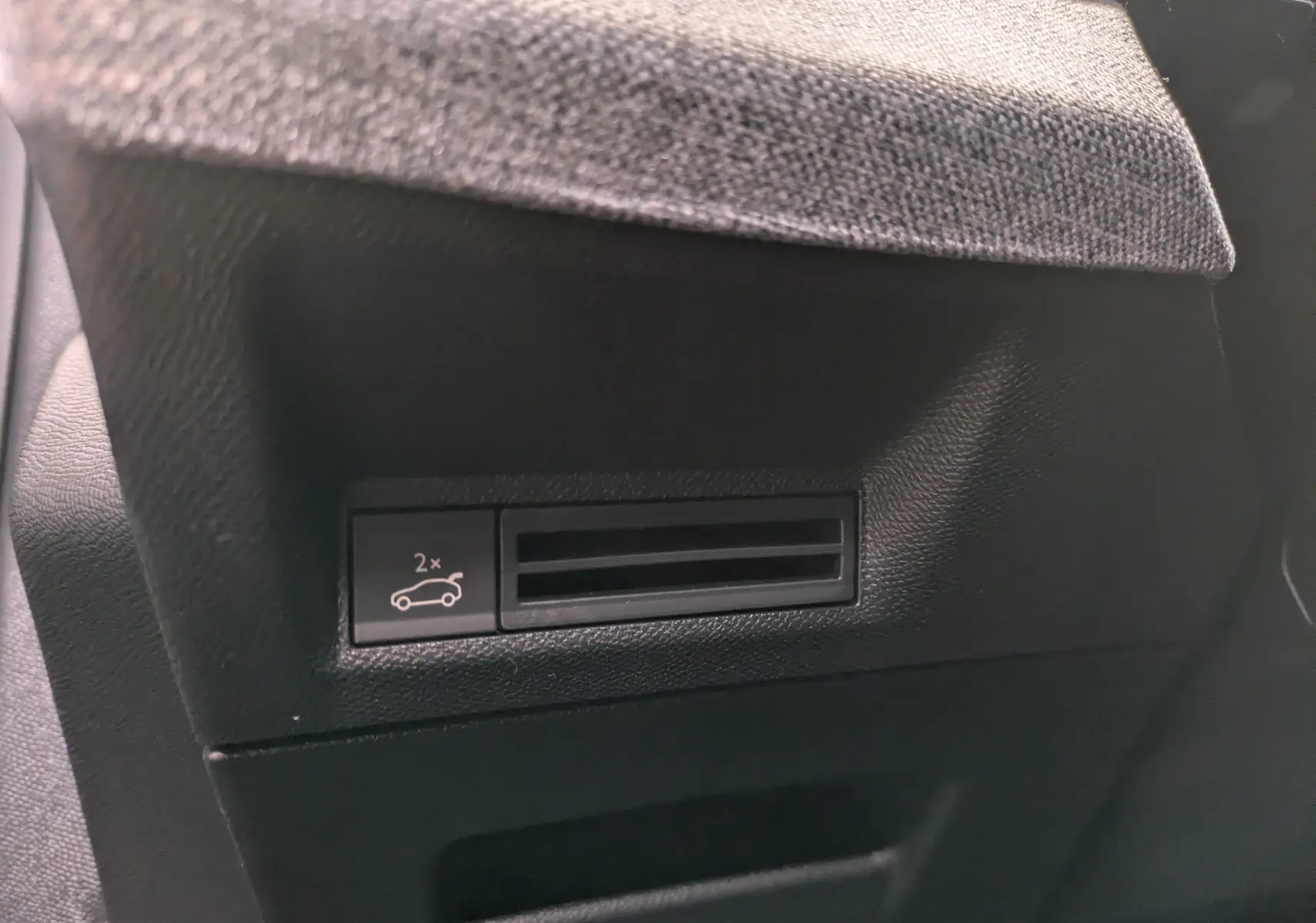 Détail du bouton d'ouverture du hayon sur la garniture intérieure noire d'un Peugeot 3008 Hybrid 145 gris titane.