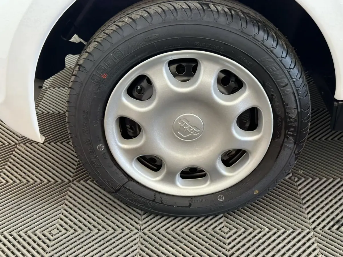 Gros plan sur la roue arrière droite d'une Aixam Minauto E Access blanche de 2025, avec pneu noir sur sol texturé.