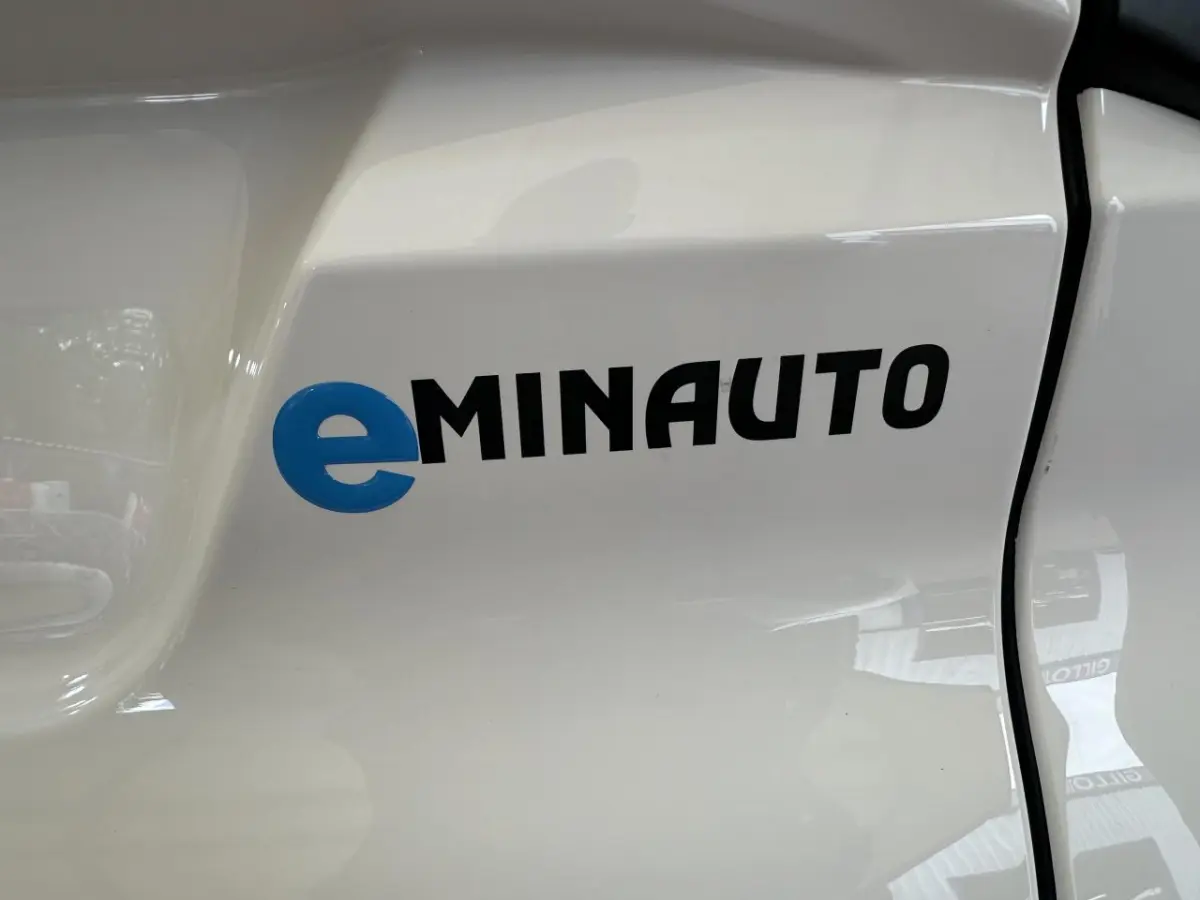 Gros plan sur le logo eMINAUTO bleu et noir sur la portière blanche côté conducteur d'une Aixam MINAUTO E ACCESS 2025 électrique.