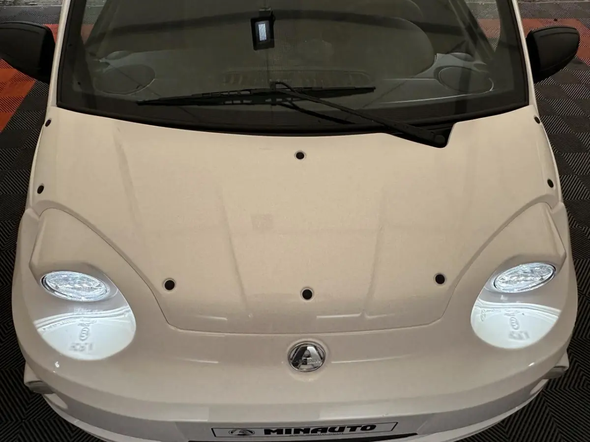 Vue plongeante sur l'avant blanc de l'AIXAM MINAUTO E ACCESS 2025 avec phares ovales et logo central visible.