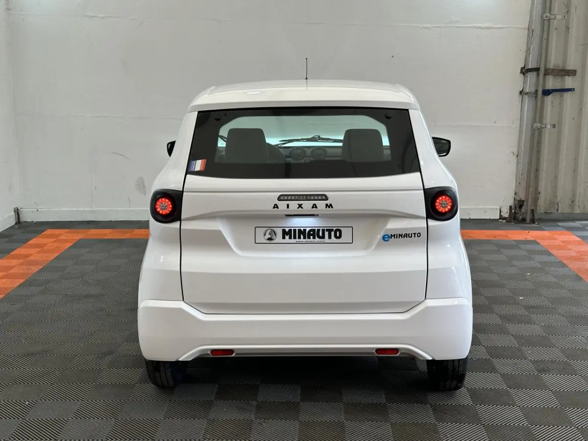 Vue arrière d'une Aixam MINAUTO E ACCESS blanche 2025 avec feux ronds allumés et logo eMINAUTO visible.