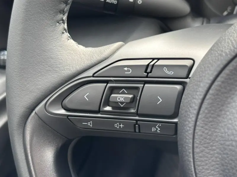 Gros plan sur les commandes multifonctions noires du volant cuir de la Toyota Yaris blanche 2025, version 116h Dynamic.