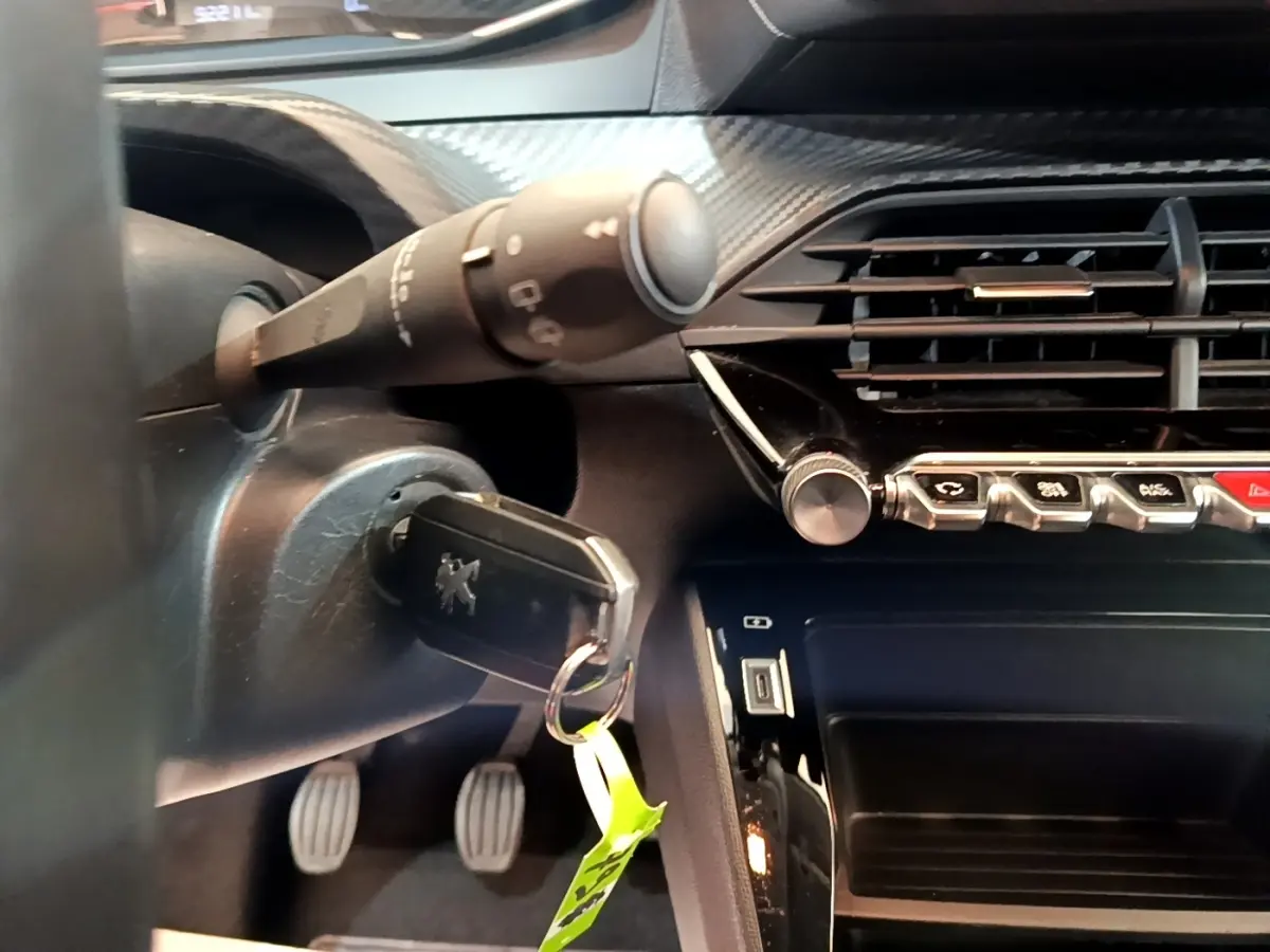 Vue rapprochée de l’intérieur côté conducteur de la Peugeot 208 blanche, avec clé insérée et commandes du tableau de bord visibles.