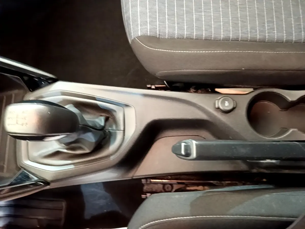 Vue plongeante sur la console centrale noire d'une Peugeot 208 blanche, avec levier de vitesse manuel et frein à main.