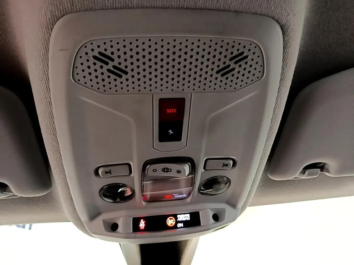 Vue en contre-plongée du plafonnier gris avec bouton SOS et éclairage intérieur de la Peugeot 208 blanche.