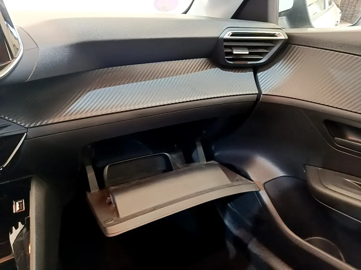 Intérieur de la Peugeot 208 2021, vue côté passager sur la boîte à gants ouverte et tableau de bord noir texturé.