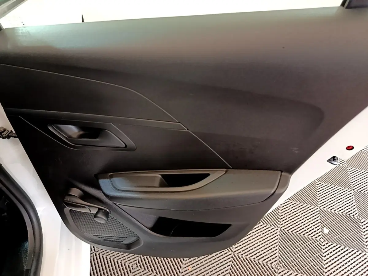 Vue rapprochée de la porte avant gauche blanche d’une Peugeot 208 2021 avec poignée et commande de vitre manuelle.