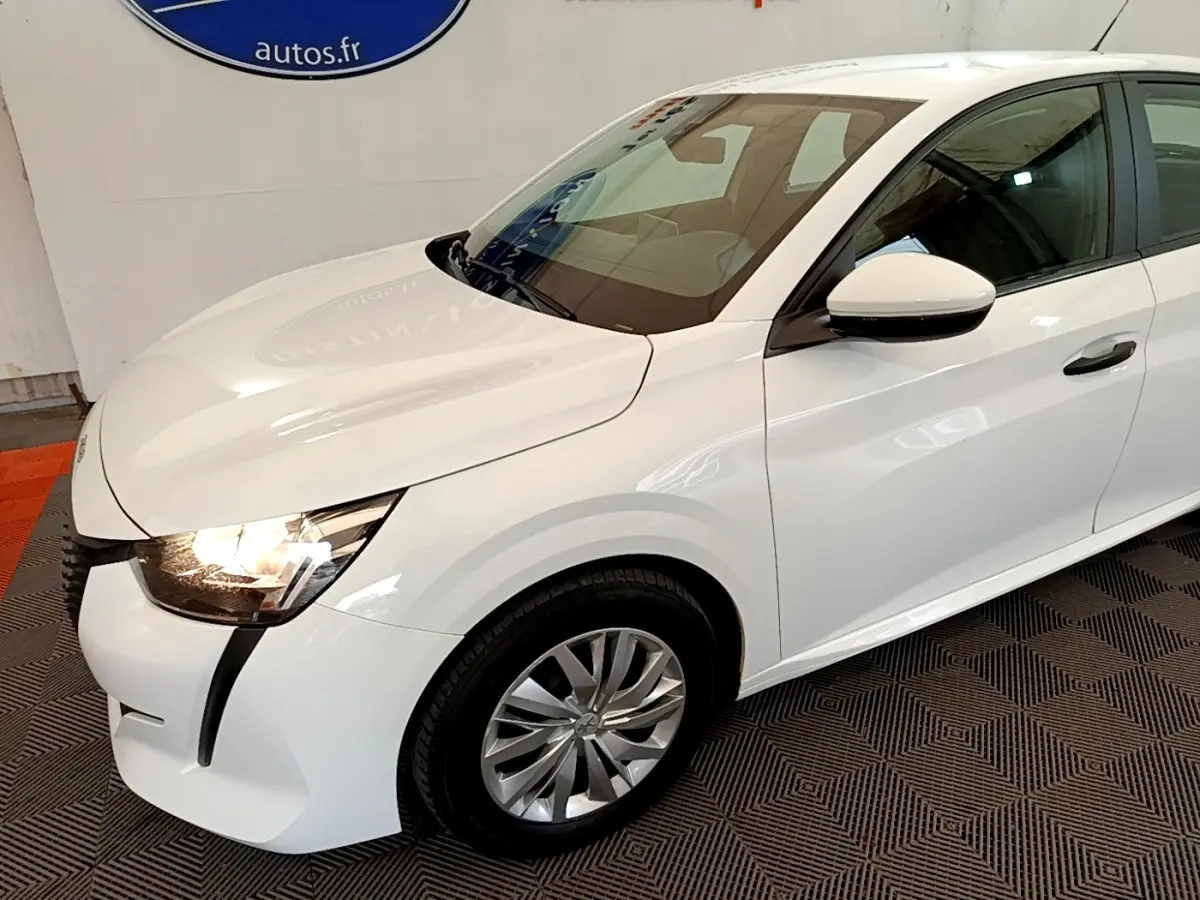 PEUGEOT 208 blanc vue 3/4 avant droit avec phares allumés et jantes alliage au sol texturé.