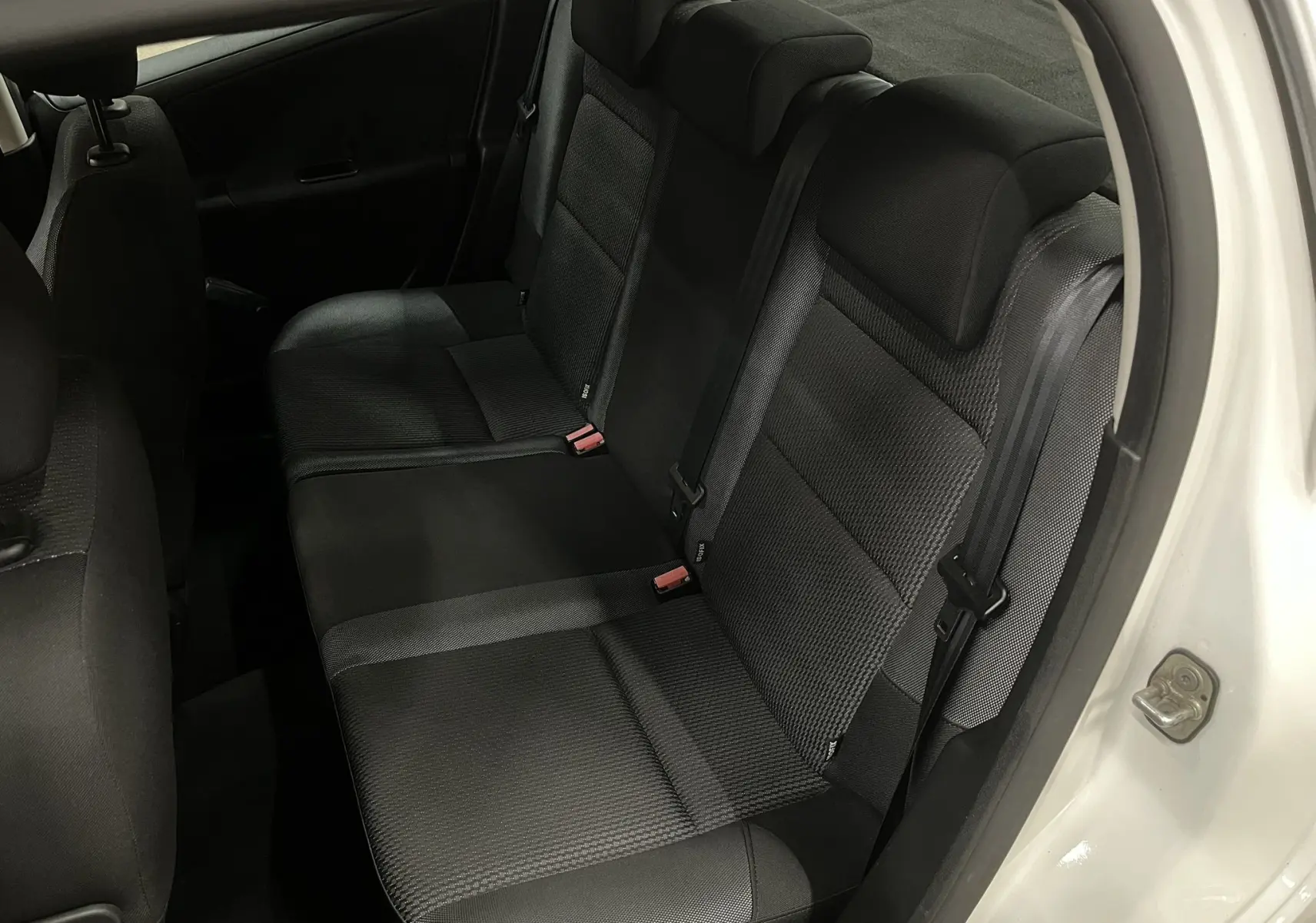 Vue intérieure côté arrière droit montrant la banquette arrière en tissu gris noir d'une Peugeot 207 blanche.