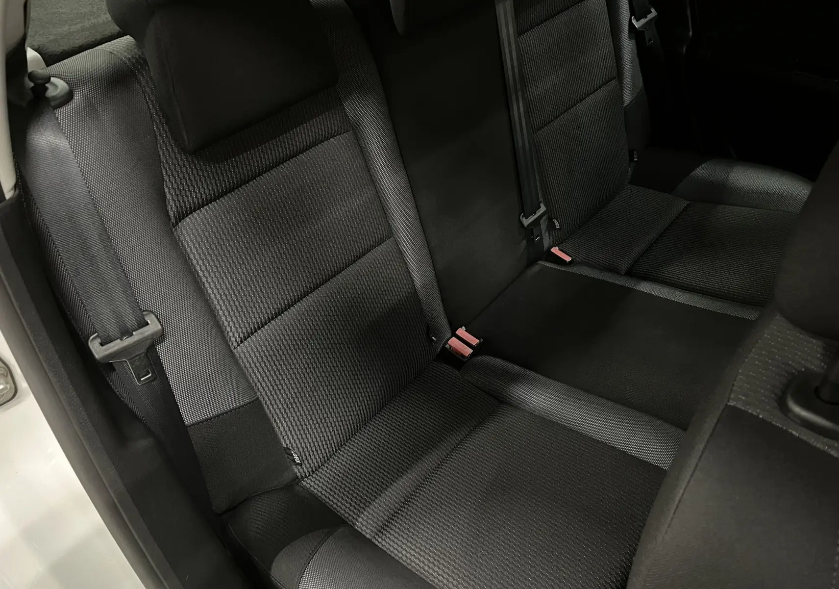 Vue rapprochée de la banquette arrière en tissu gris noir de la Peugeot 207 Active 2011, avec ceintures de sécurité visibles.