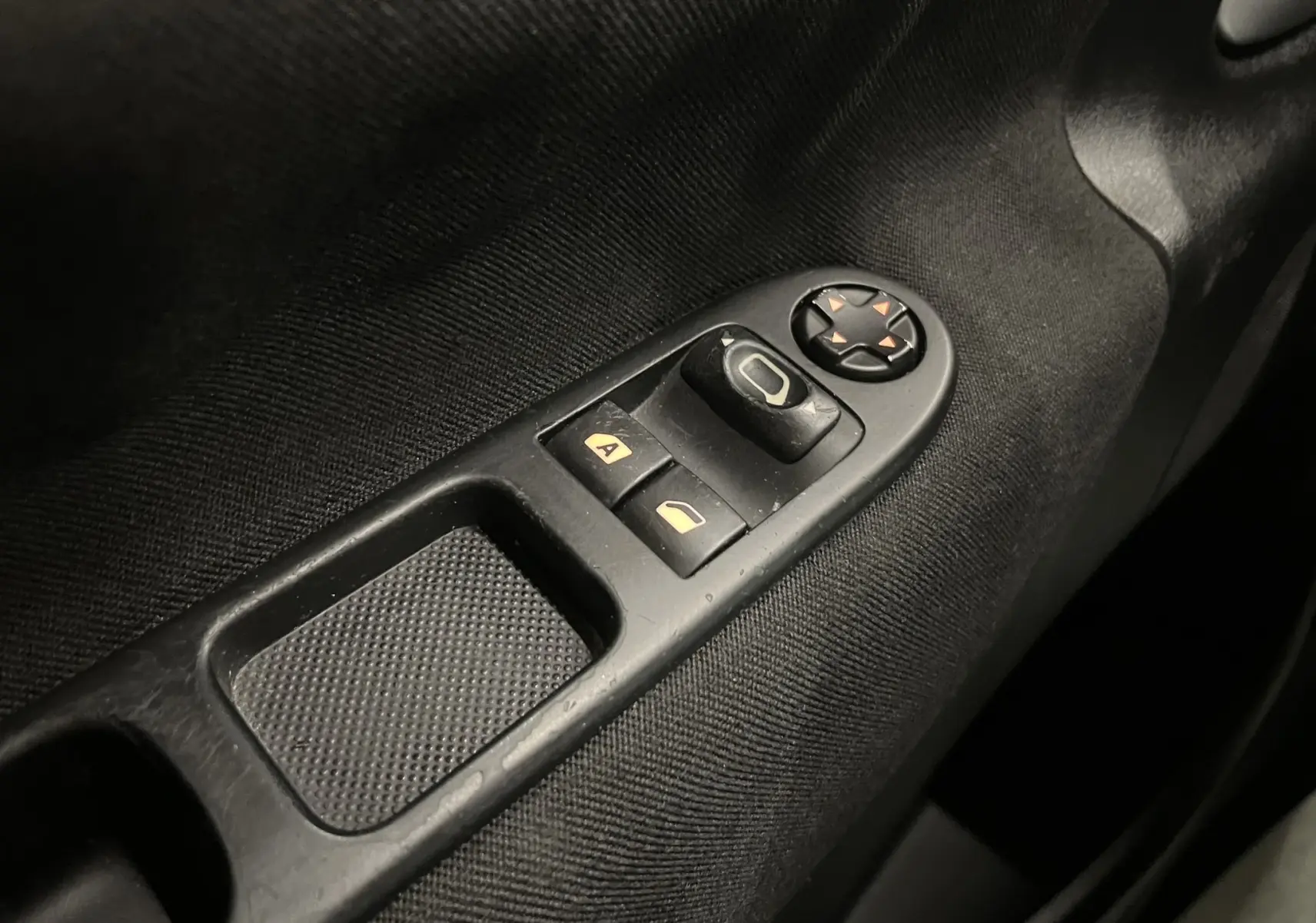 Gros plan sur les commandes de lève-vitres et réglage des rétroviseurs côté conducteur d’une Peugeot 207 blanche de 2011.