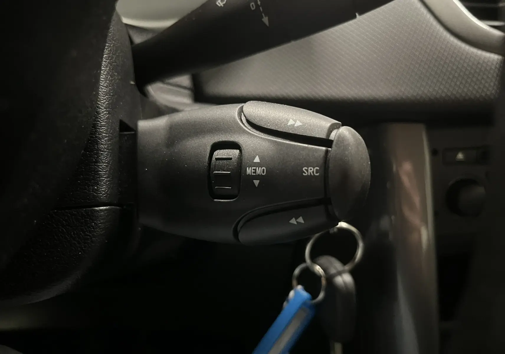 Gros plan sur la commande au volant côté gauche de la Peugeot 207 Active 2011, avec clé et intérieur gris noir visible.