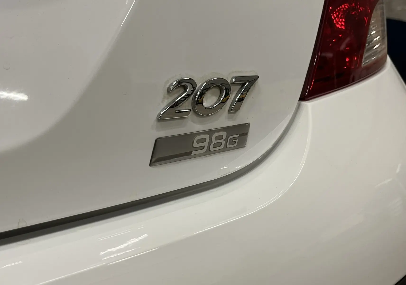 Gros plan sur l'arrière droit blanc d'une Peugeot 207 avec le logo 207 et l'insigne finition 98G visible.
