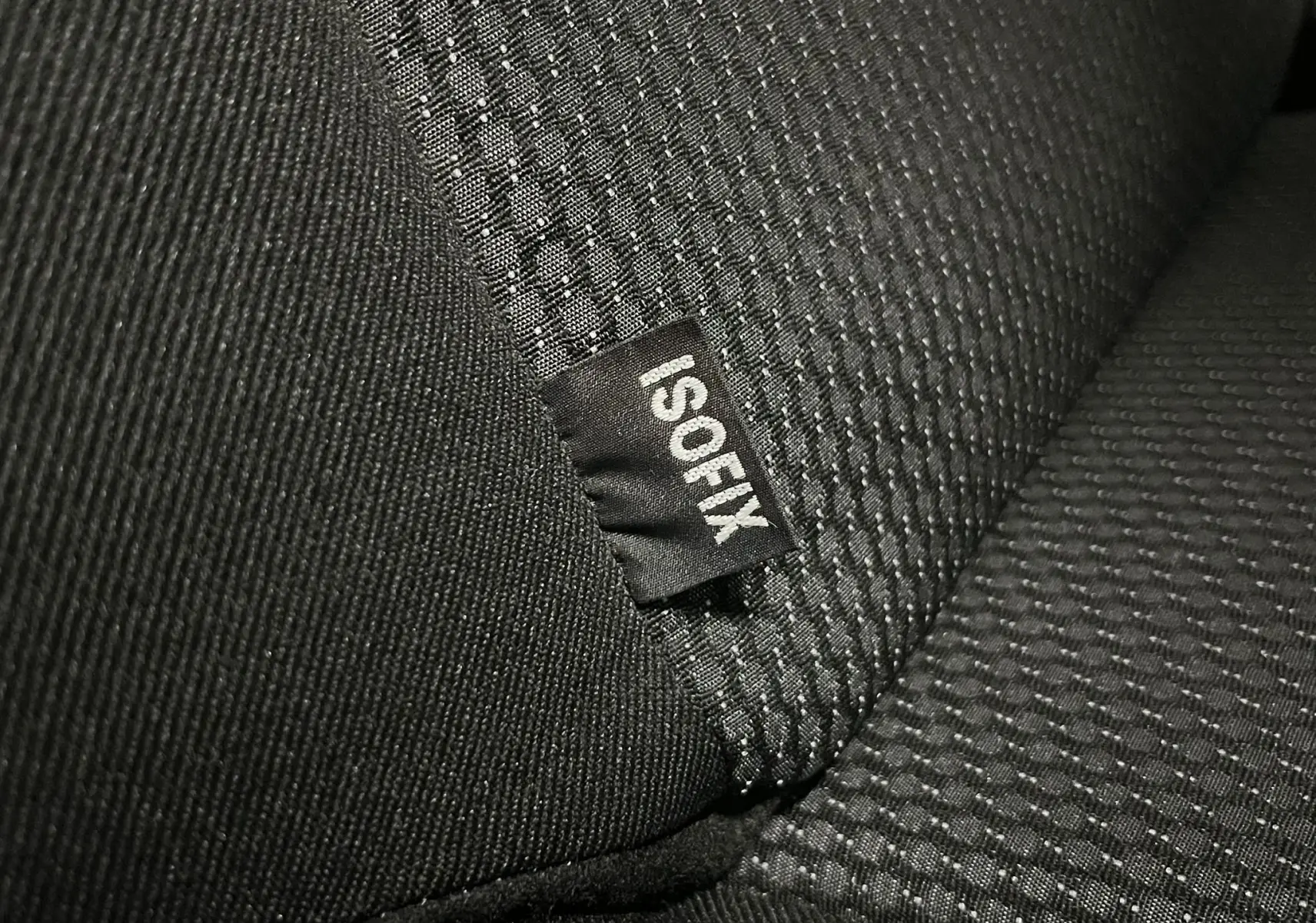 Gros plan sur l’étiquette ISOFIX cousue sur la banquette arrière en tissu gris noir de la Peugeot 207 Active 2011.