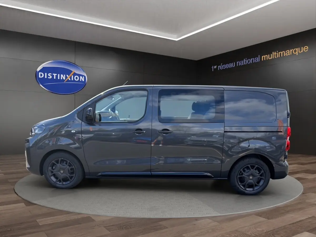 Profil droit d’un Citroën Jumpy gris foncé 2026 avec vitres latérales et jantes noires en showroom.