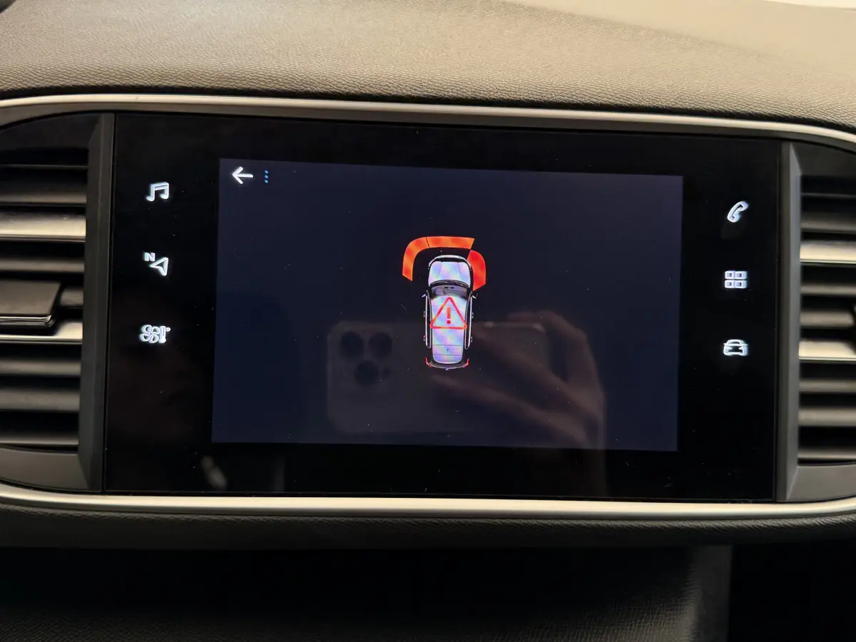 Écran tactile central de la Peugeot 308 blanc montrant une alerte de capteurs de stationnement avant.