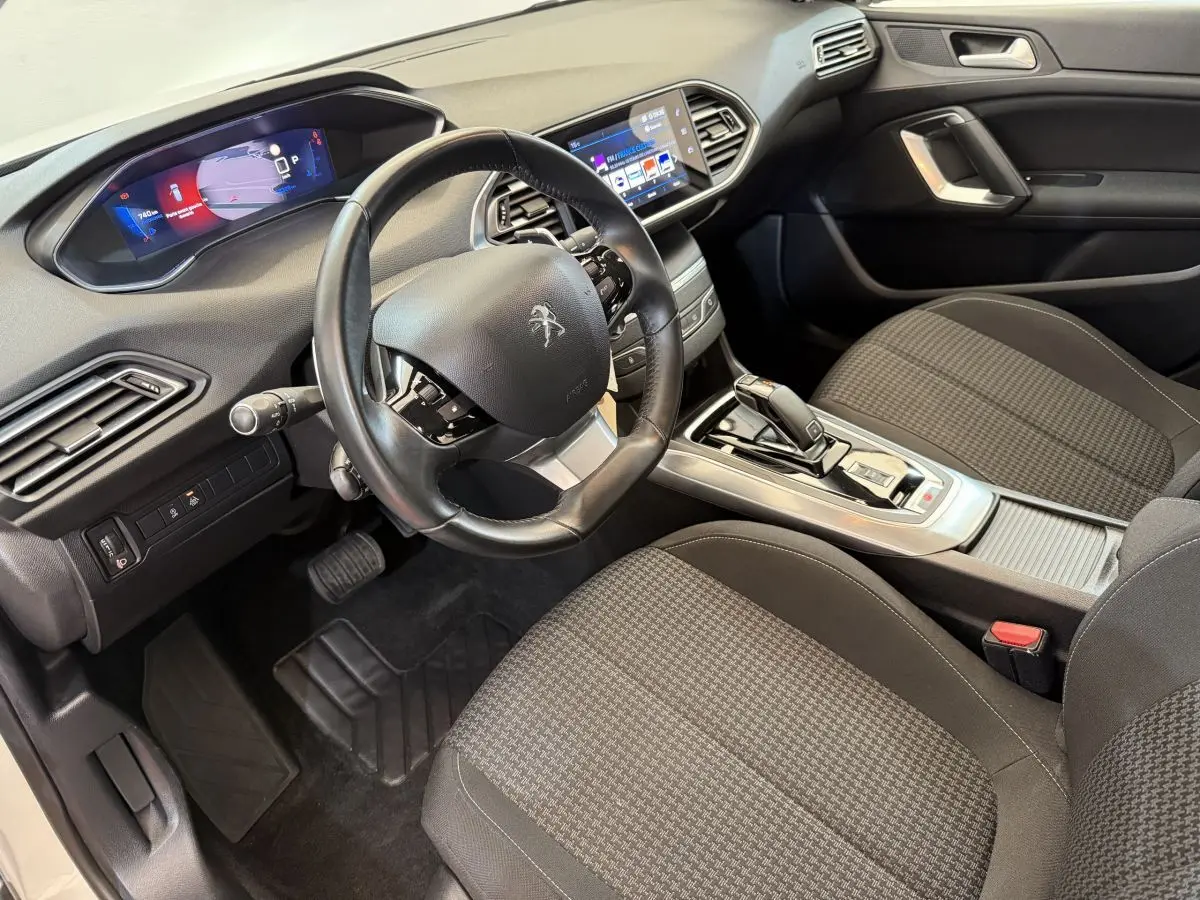 Intérieur de la Peugeot 308 2021 vu côté conducteur, volant cuir, écran tactile et sièges tissu gris à motifs.