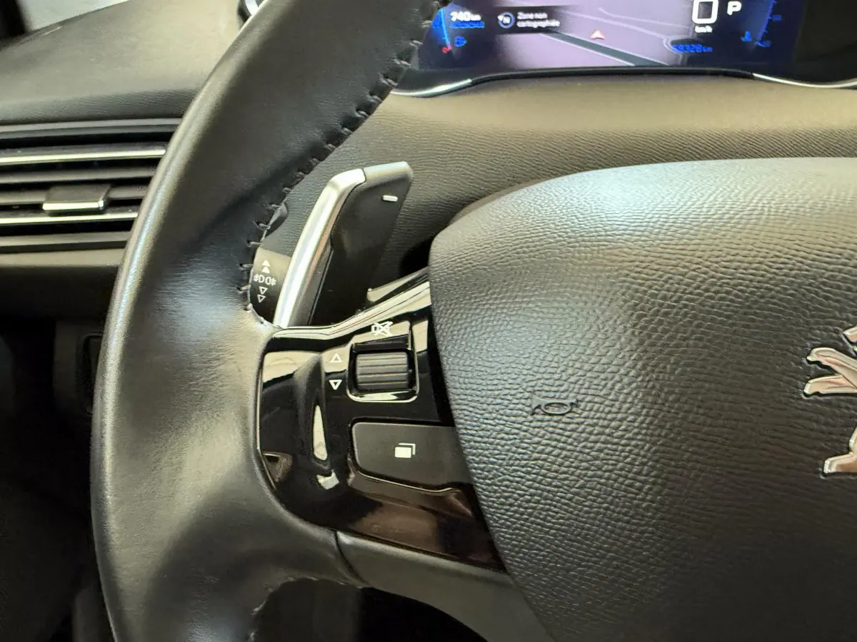 Gros plan sur le volant cuir noir de la Peugeot 308 2021 avec commandes intégrées et tableau de bord numérique visible.