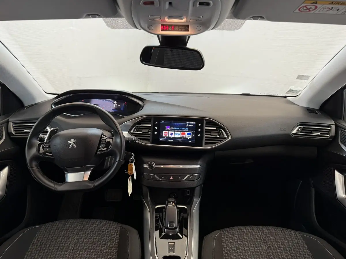 Vue frontale de l'intérieur noir de la Peugeot 308 2021 avec volant cuir, écran tactile central et tableau de bord digital.