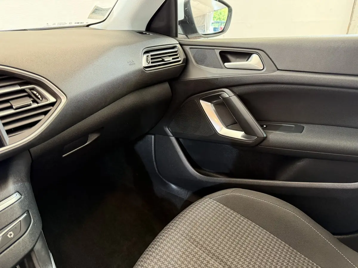 Vue intérieure côté passager de la Peugeot 308 blanche, mettant en valeur la porte et le tableau de bord noir.