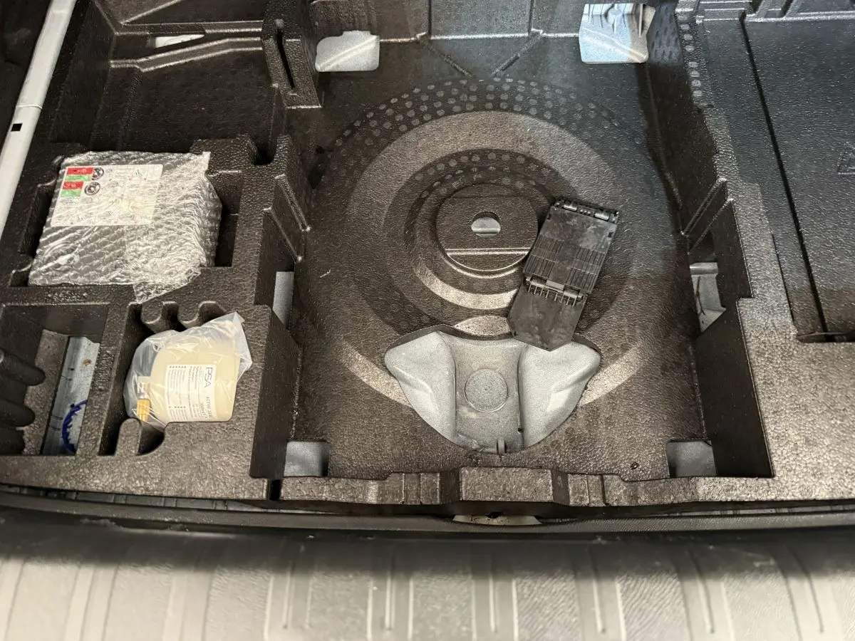 Vue plongeante sur le compartiment de rangement sous le plancher du coffre d'une Peugeot 308 blanche, avec accessoires intégrés.