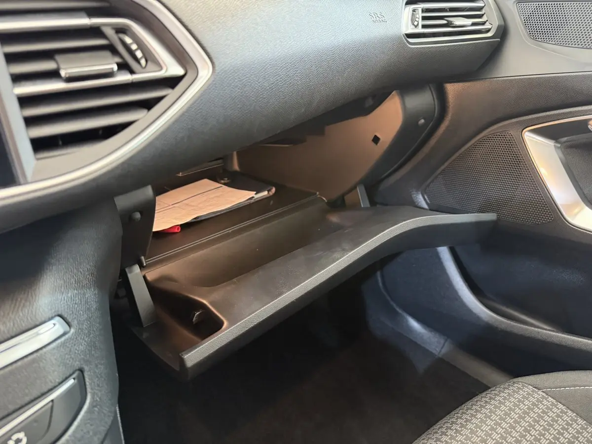 Gros plan sur la boîte à gants ouverte côté passager du Peugeot 308 2021, intérieur noir avec documents visibles.
