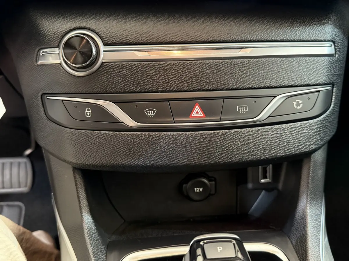 Gros plan sur la console centrale noire de la Peugeot 308 avec boutons de verrouillage, hazard et prise 12V visible.