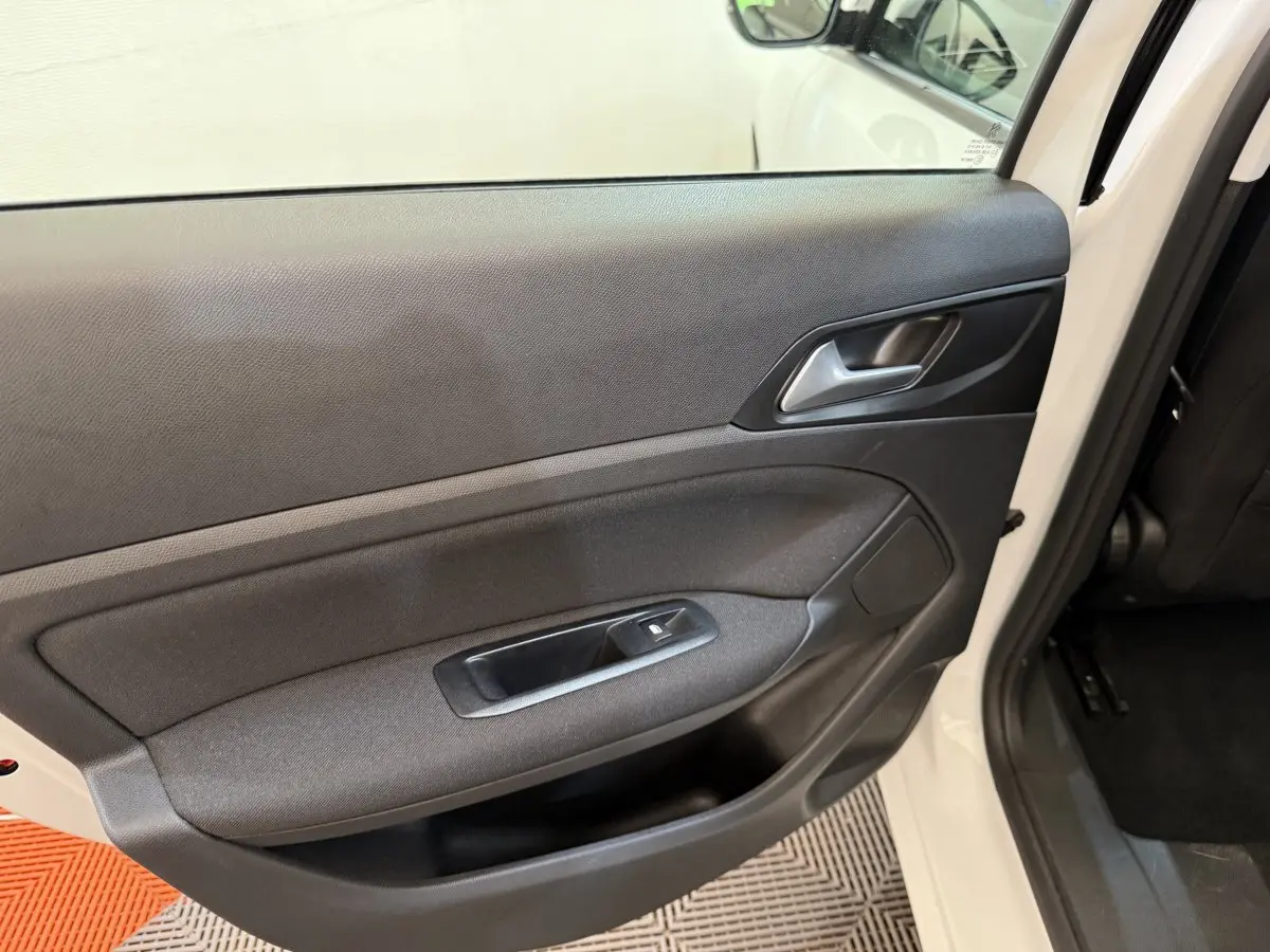 Vue intérieure de la porte arrière gauche d'une Peugeot 308 blanche, avec panneau noir et commande de vitre électrique.