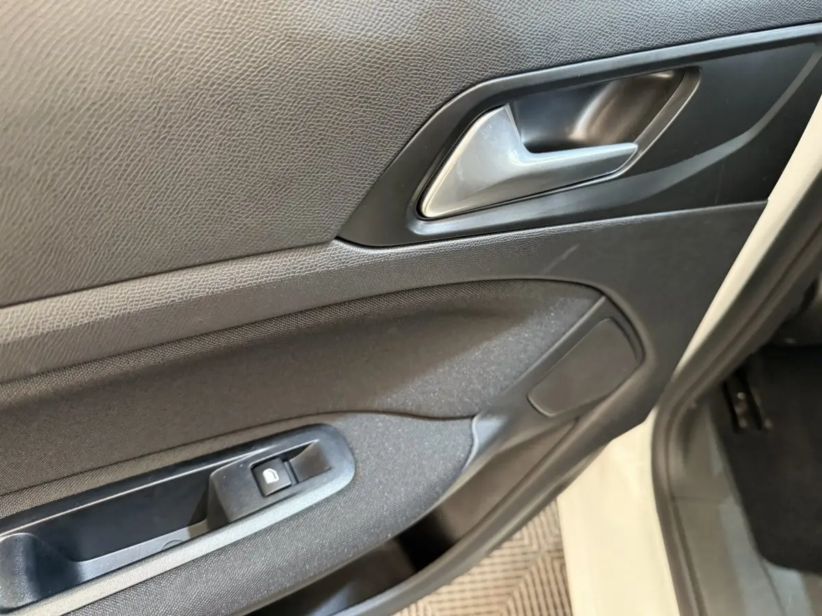 Gros plan sur la porte intérieure côté conducteur d'une Peugeot 308 blanche, avec poignée argentée et bouton de verrouillage.