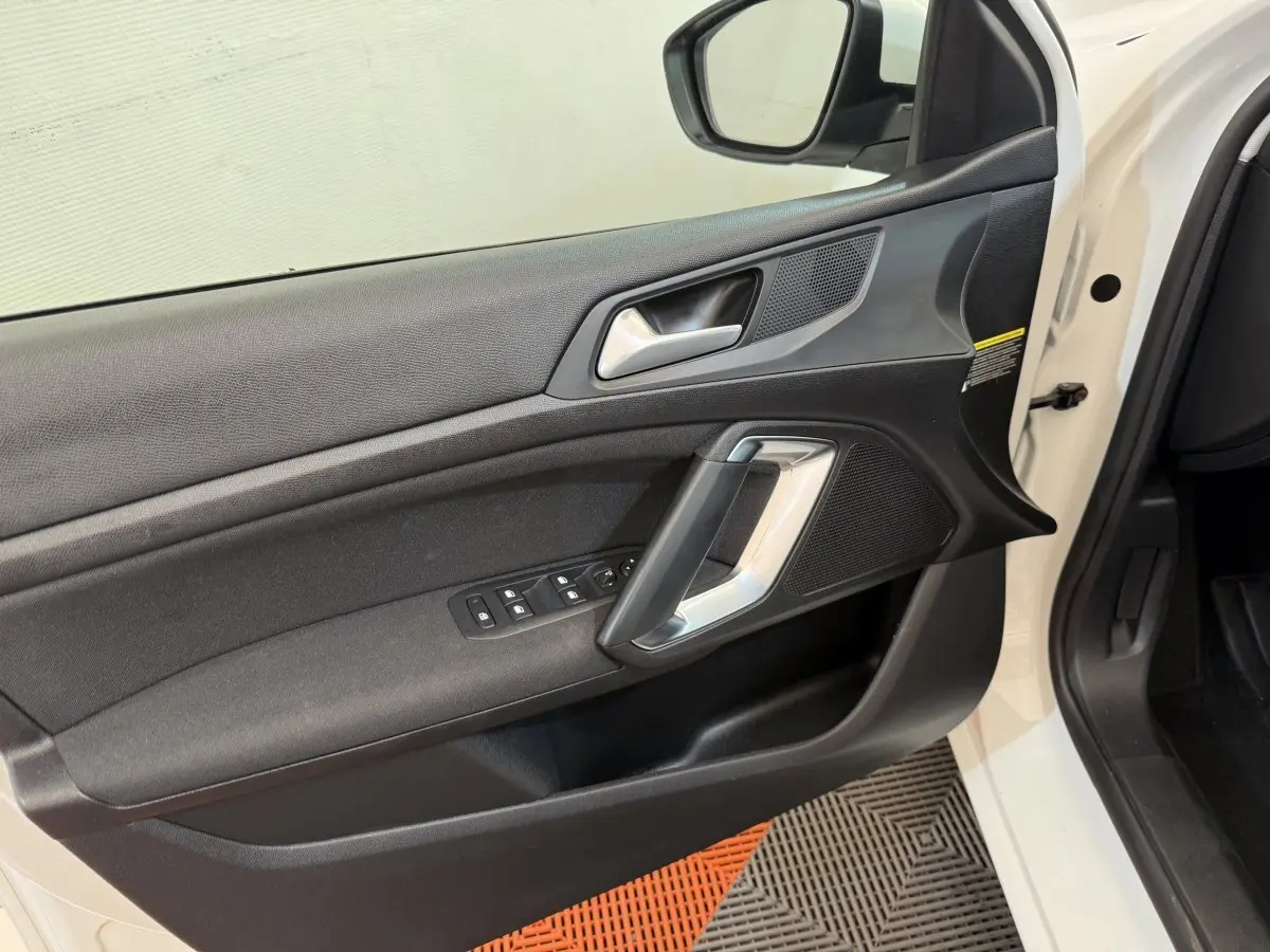 Vue intérieure de la porte avant gauche noire avec poignée argentée et commandes des vitres d'une Peugeot 308 blanche 2021