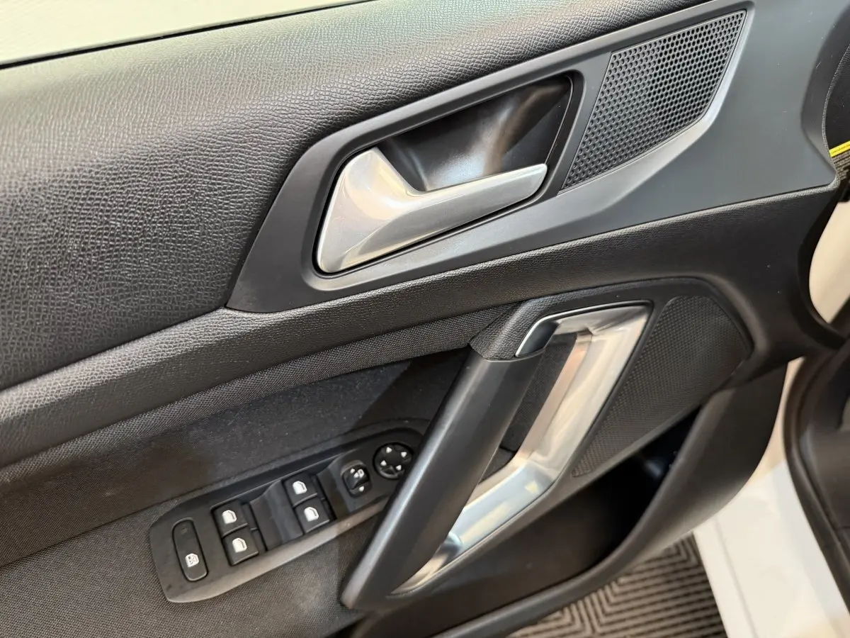 Gros plan sur la porte côté conducteur de la Peugeot 308 blanche, montrant la poignée argentée et les commandes des vitres.