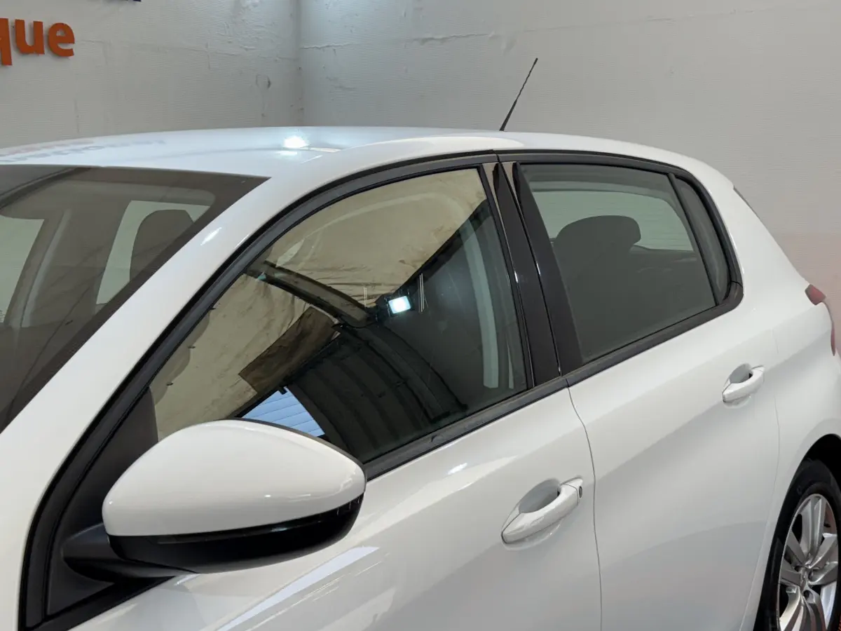 Vue latérale côté gauche d'une Peugeot 308 blanche, mettant en valeur les vitres teintées et les rétroviseurs blancs.