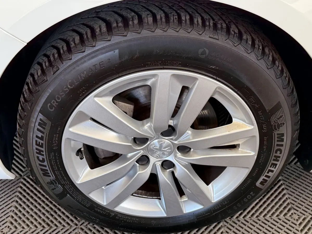 Gros plan sur la roue avant gauche d'une Peugeot 308 blanche, mettant en valeur la jante alliage et le pneu Michelin.