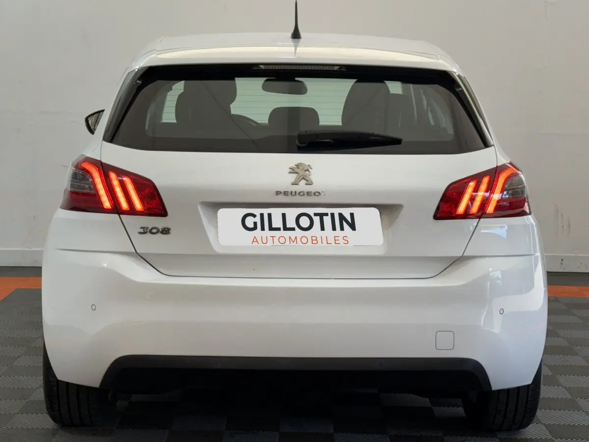 Vue arrière d'une Peugeot 308 blanche de 2021 avec feux arrière allumés et logo Peugeot visible.