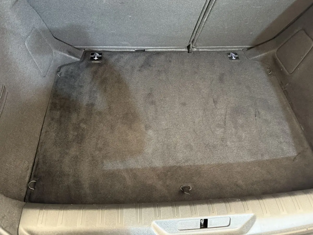Coffre vide en vue plongeante d'une Peugeot 308 blanche, tapis de sol gris foncé et crochets d'arrimage visibles.