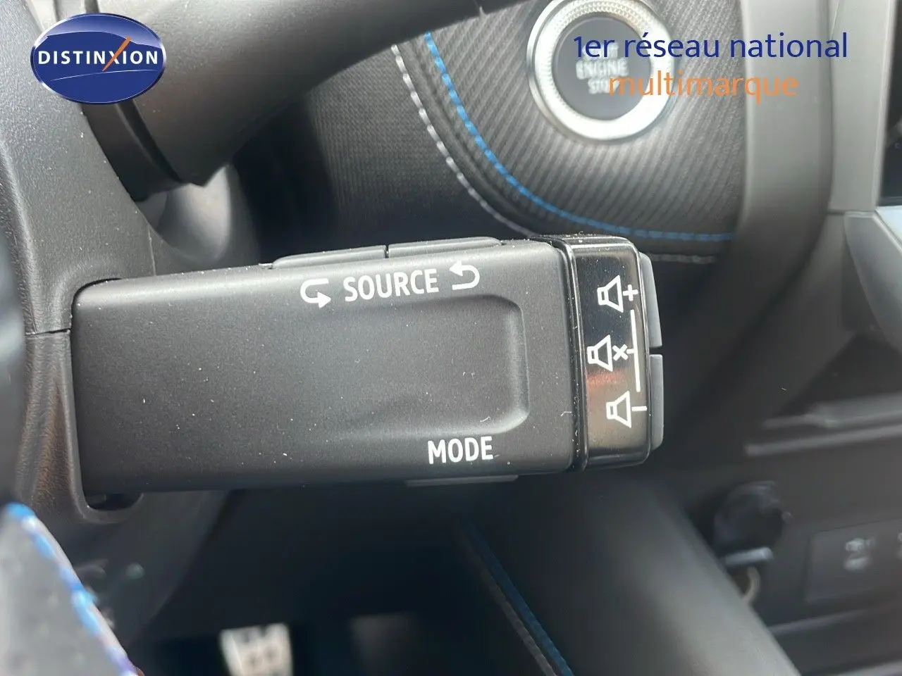 Gros plan sur la commande au volant du Renault Captur E-Tech hybride 2025, avec surpiqûres bleues visibles en arrière-plan.