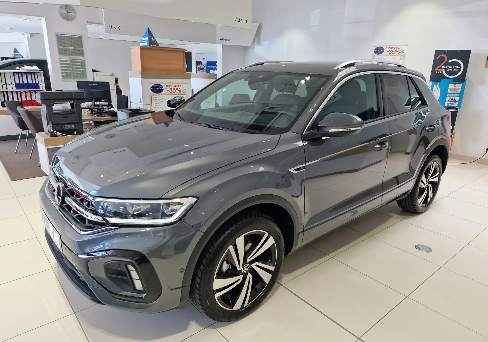Volkswagen T-Roc gris Indium Metal en 3/4 avant droit, avec jantes bi-ton et finitions R-Line visibles en showroom.