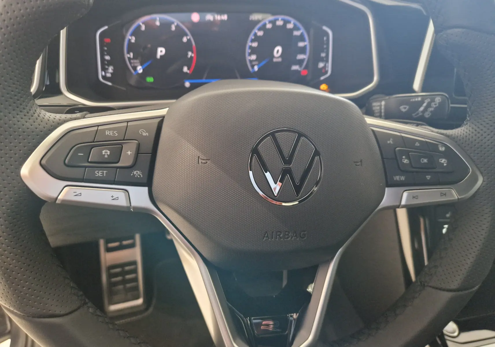 Vue rapprochée du volant multifonction noir perforé du Volkswagen T-Roc 2025 avec tableau de bord numérique en arrière-plan.